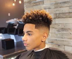 Man with a high fade haircut; brown curly hair on top. He's in a barber shop, turned sideways, and staring left.