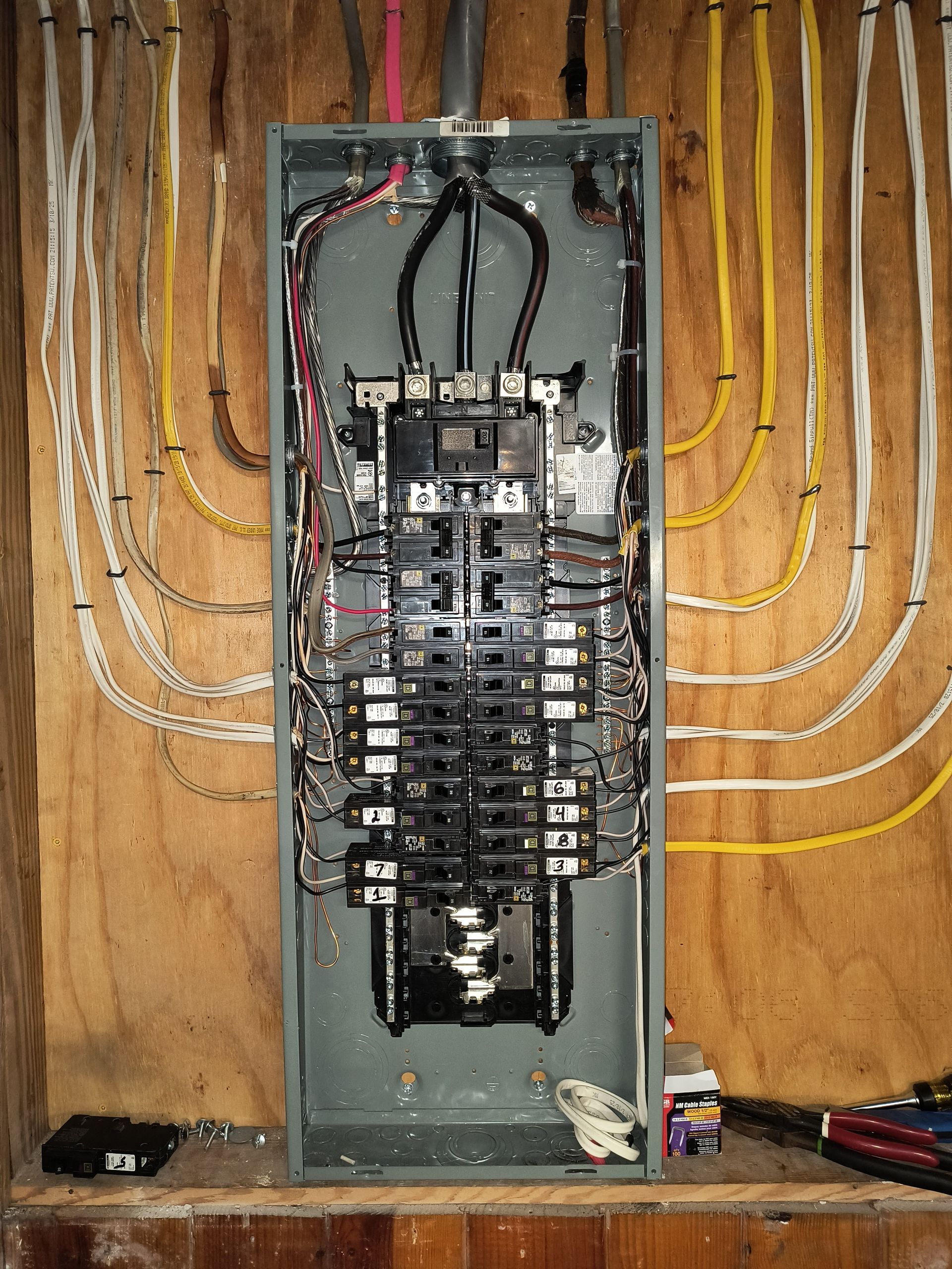 Open electrical breaker panel with exposed wiring in unfinished wall cavity