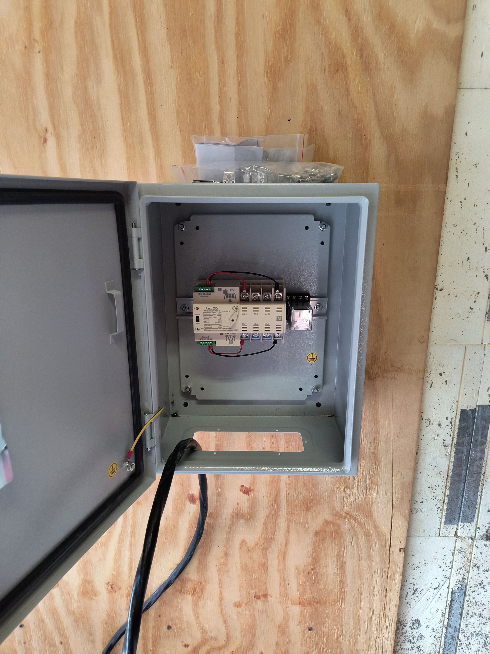Open electrical panel with meter and wires mounted on plywood wall