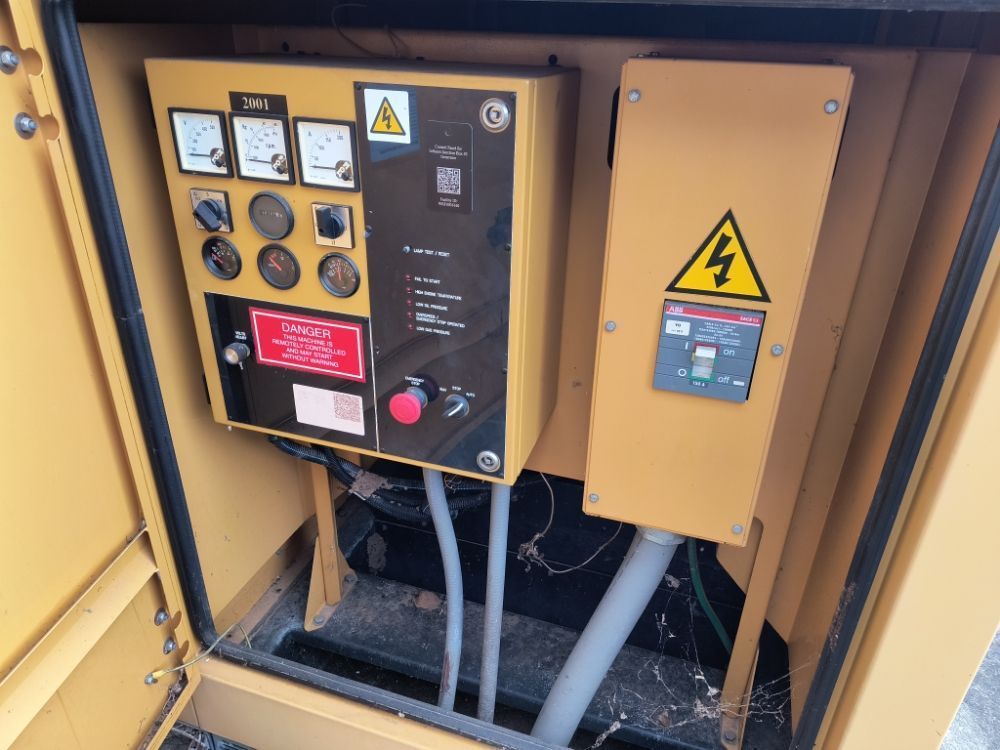 Yellow industrial control panel with gauges, switches, and electrical warning signs inside equipment cabinet