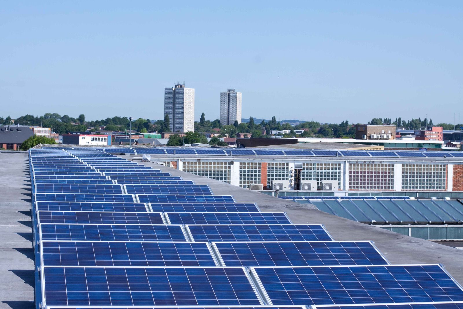 Solar panels covering a rooftop with city buildings in the background under a clear blue sky