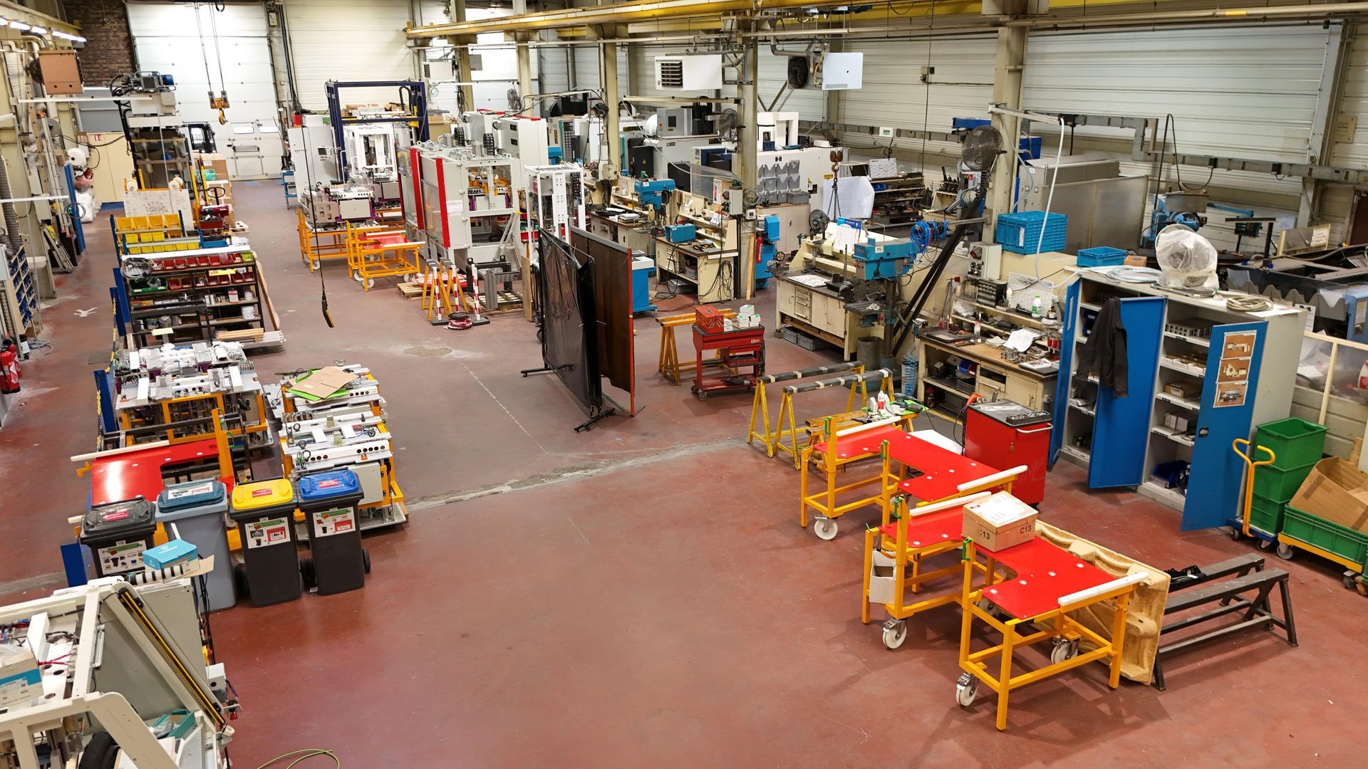 Plan large d'un atelier de fabrication rempli de machines, d'établis, d'outils et de chariots rouges.