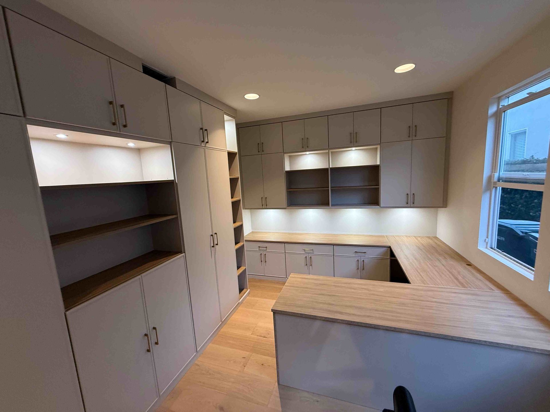 Home office with light gray cabinets, wooden desk, and shelves.
