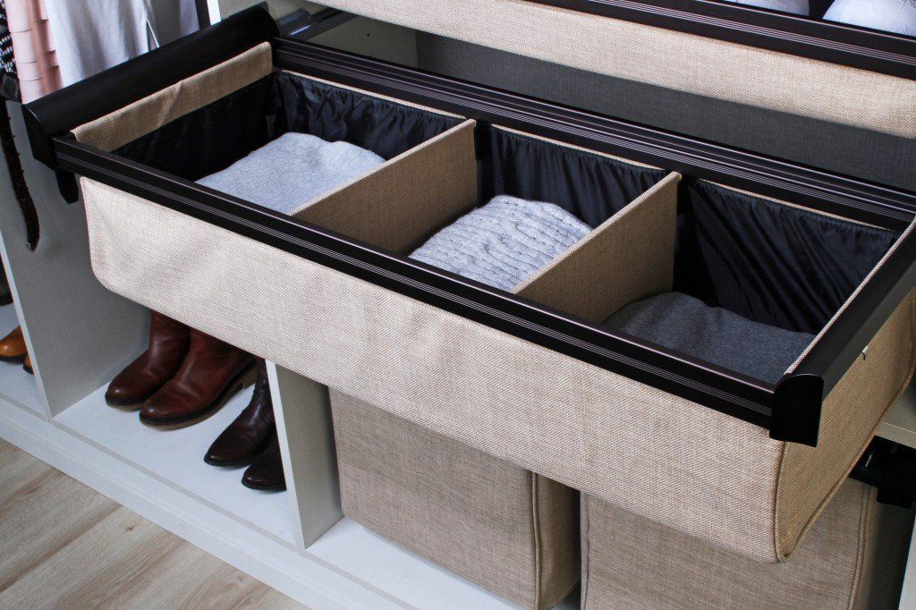 Closet organizer with three divided bins. Tan fabric exterior, black trim, storing folded clothes.