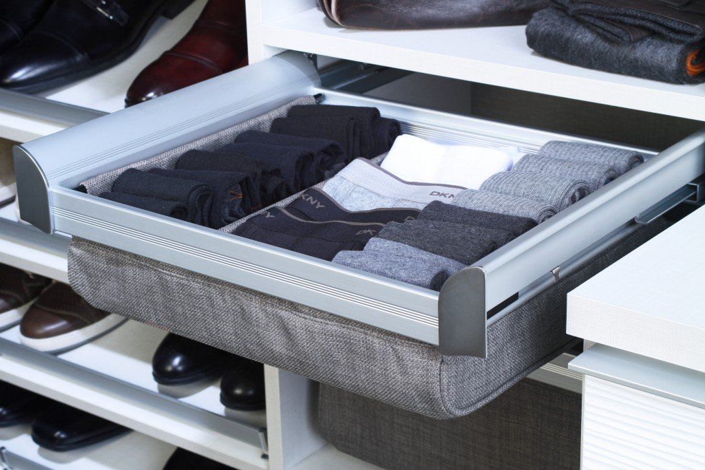 Open gray drawer organizer with folded clothes and compartments in a closet shelf