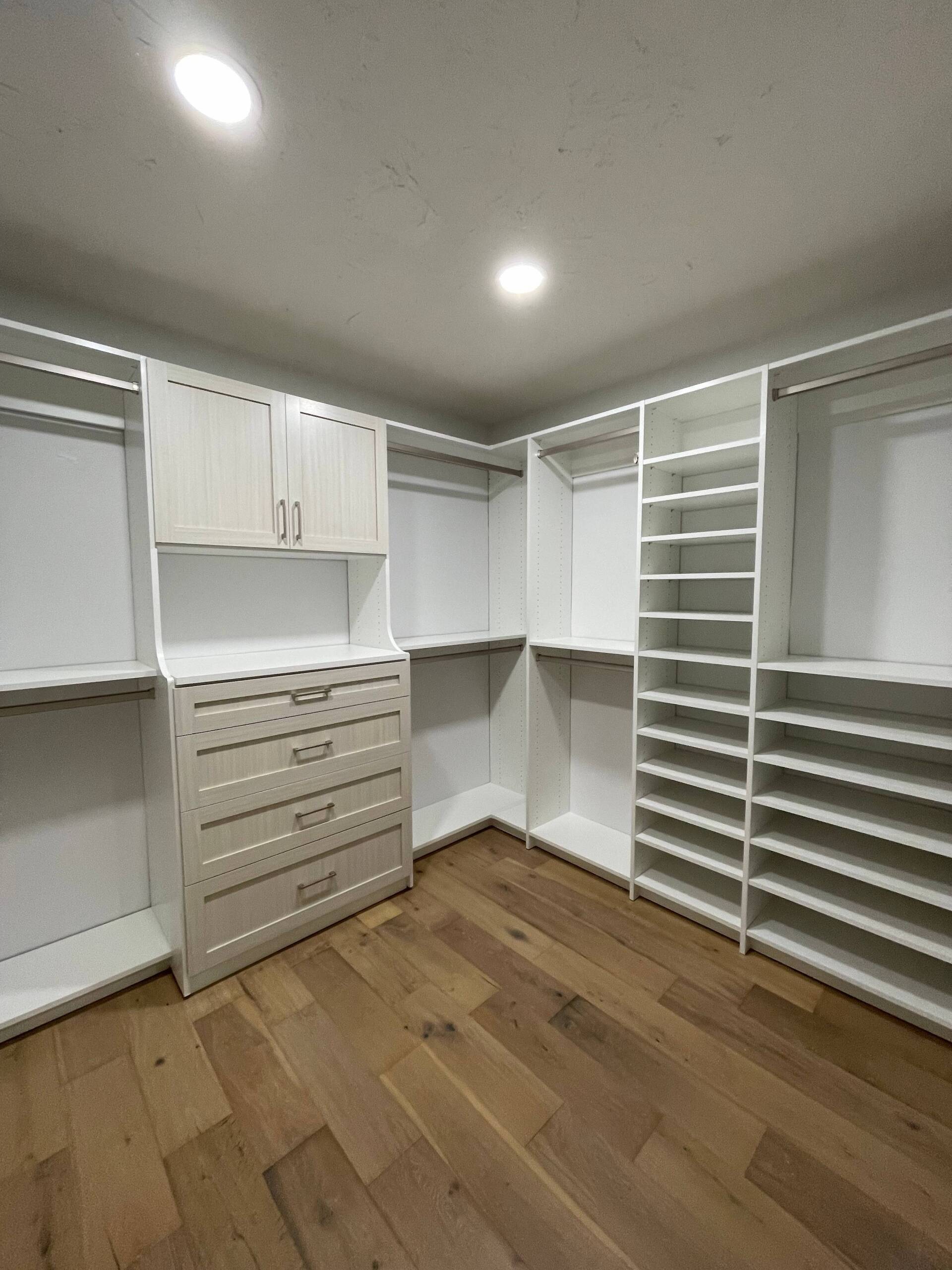 a walk in closet with wooden floors and white cabinets .