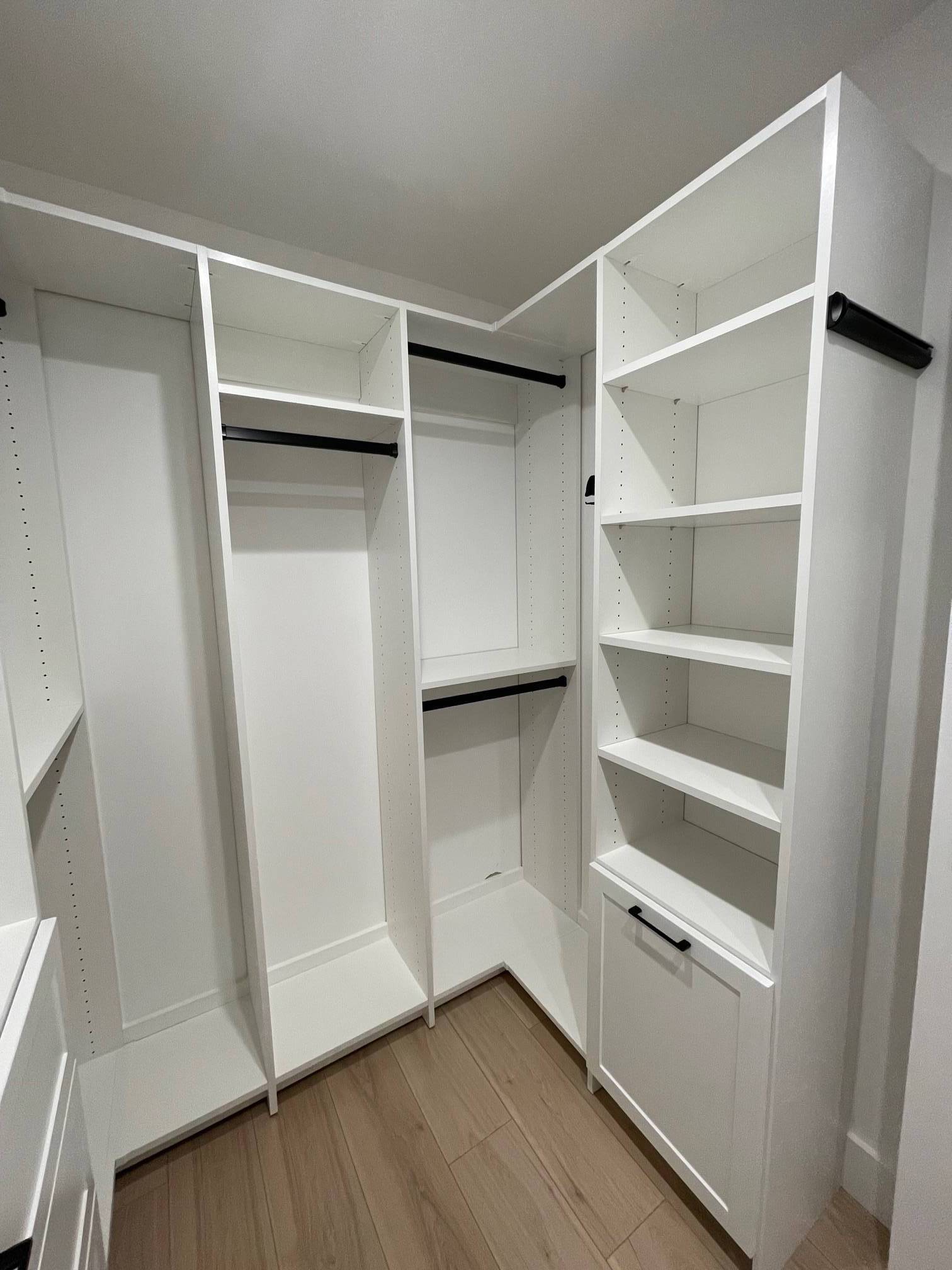 a white finish walk in closet with lots of shelves and clothes racks .