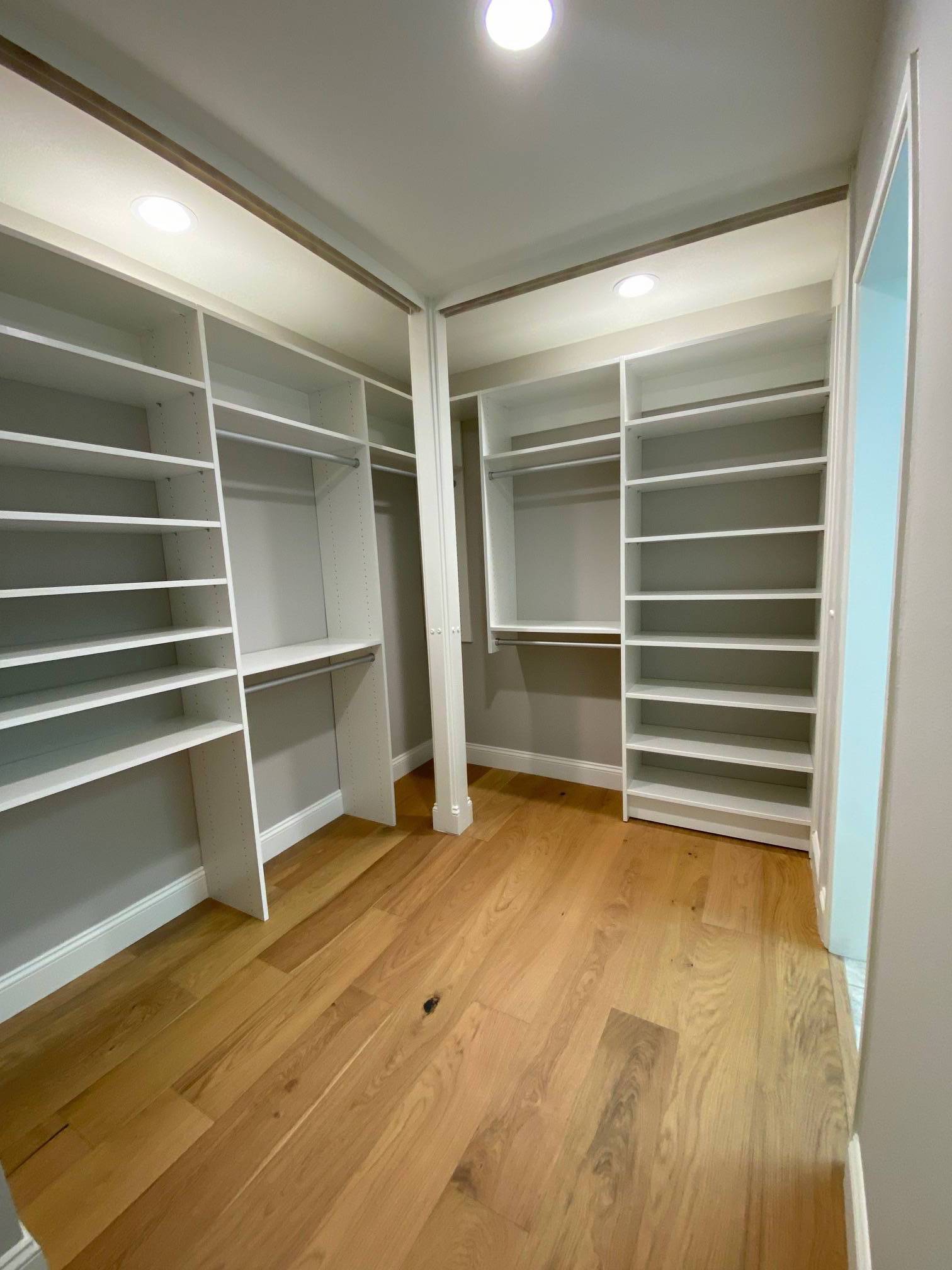 a walk in closet with hardwood floors and white shelves .