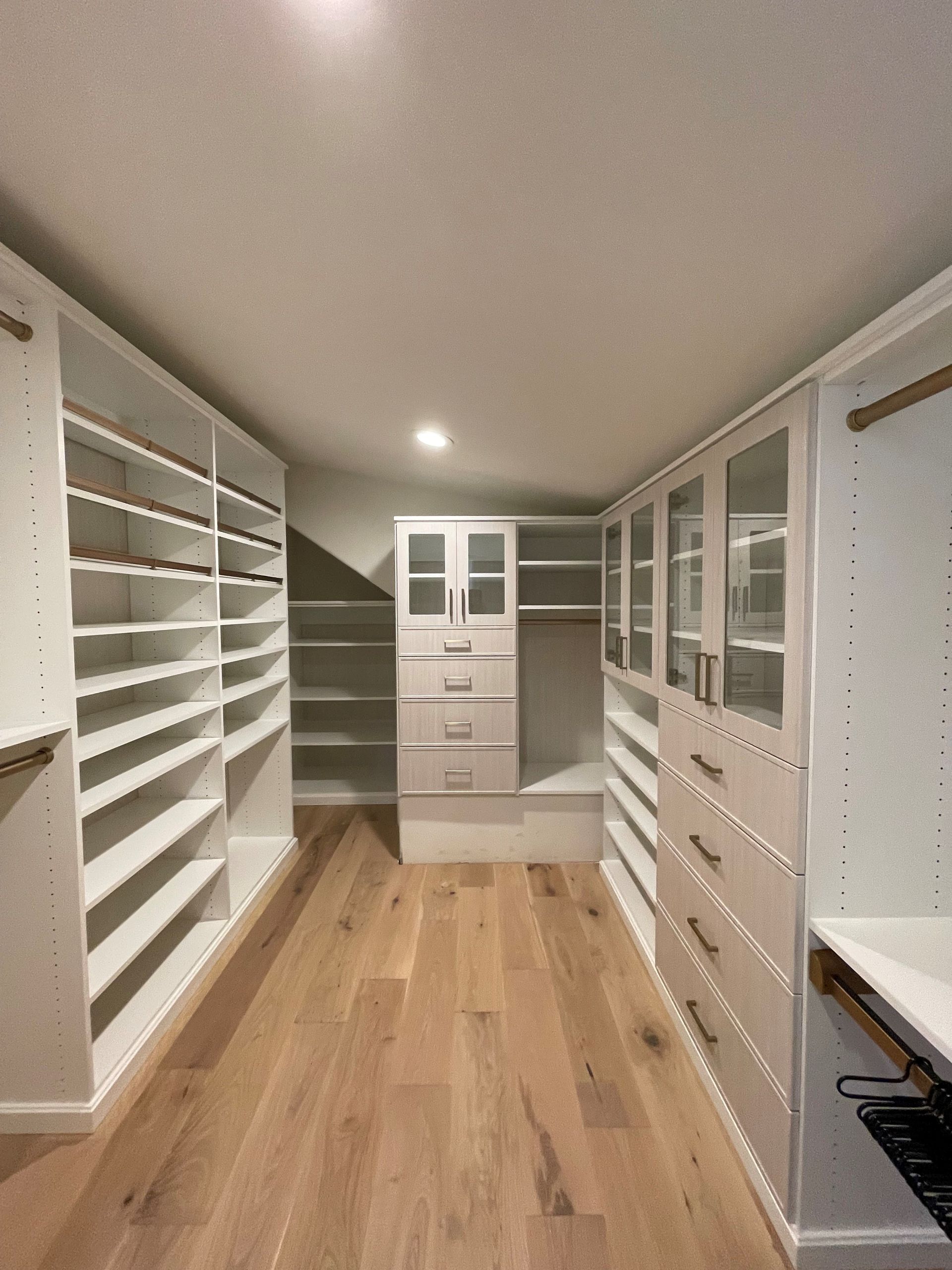 a white finish custom walk in closet with lots of shelves and drawers .