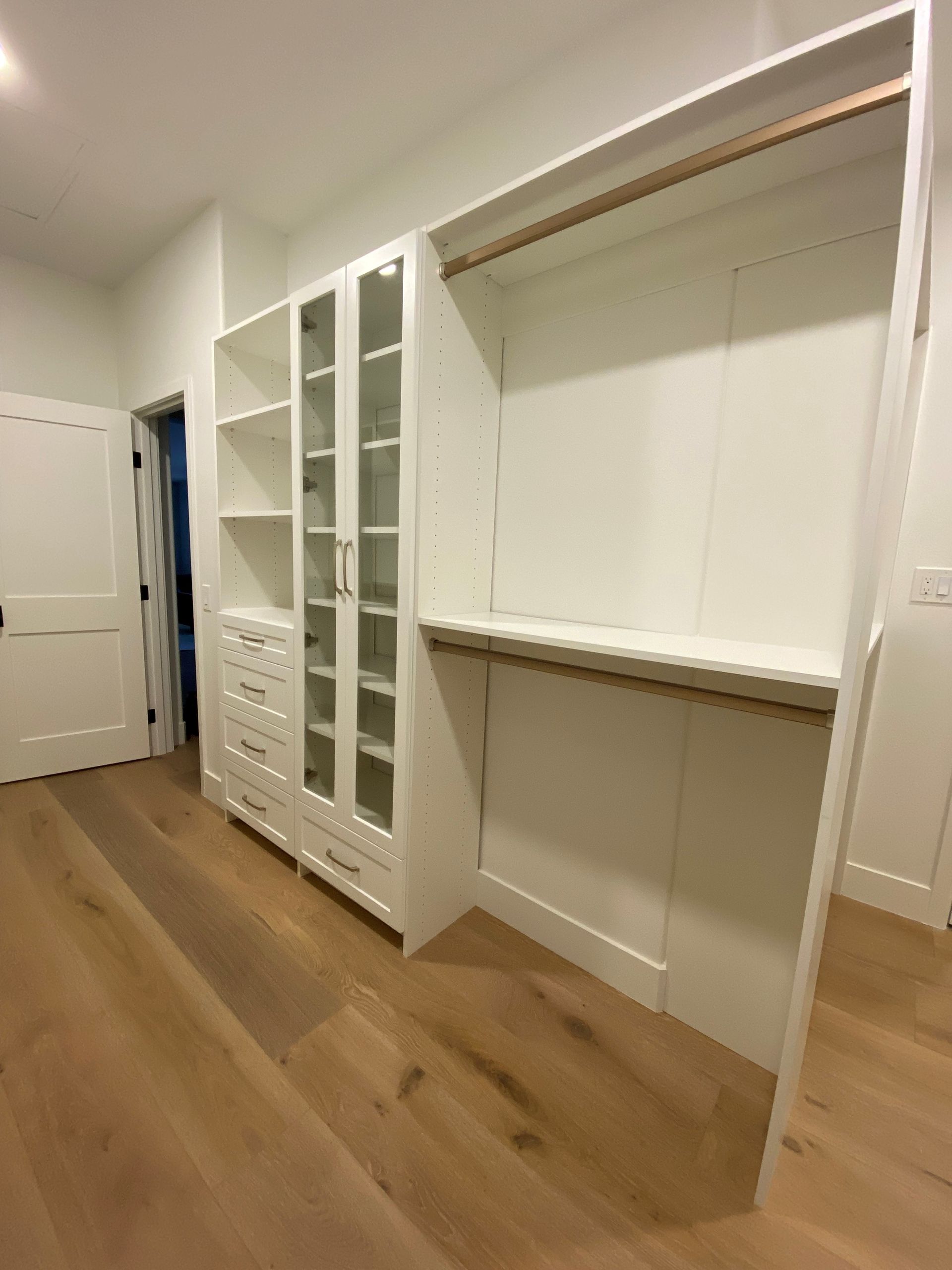 a walk in closet with hardwood floors and white cabinets .