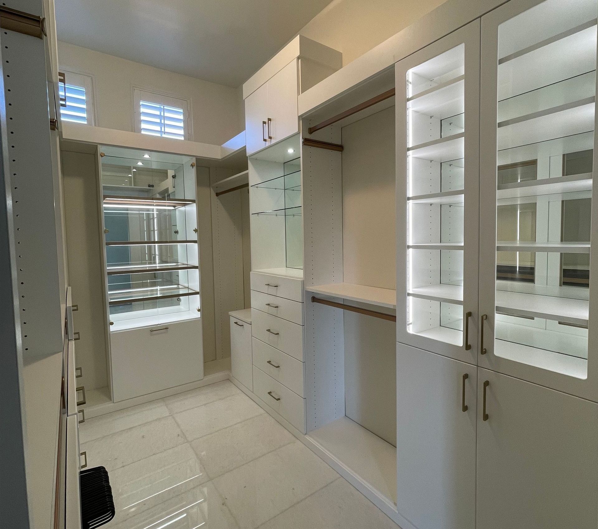 a walk in closet with white cabinets and glass doors