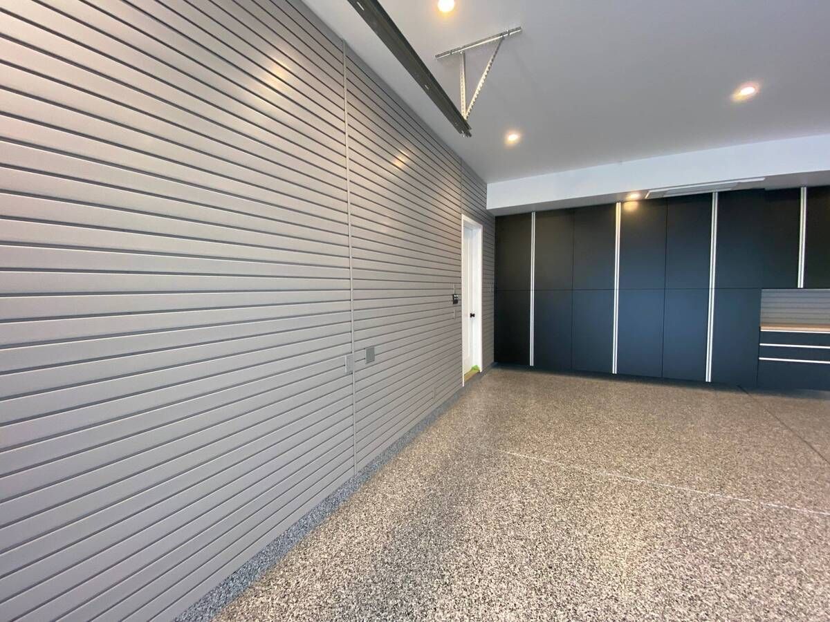 an empty garage with a gray slatwall and basalt cabinets