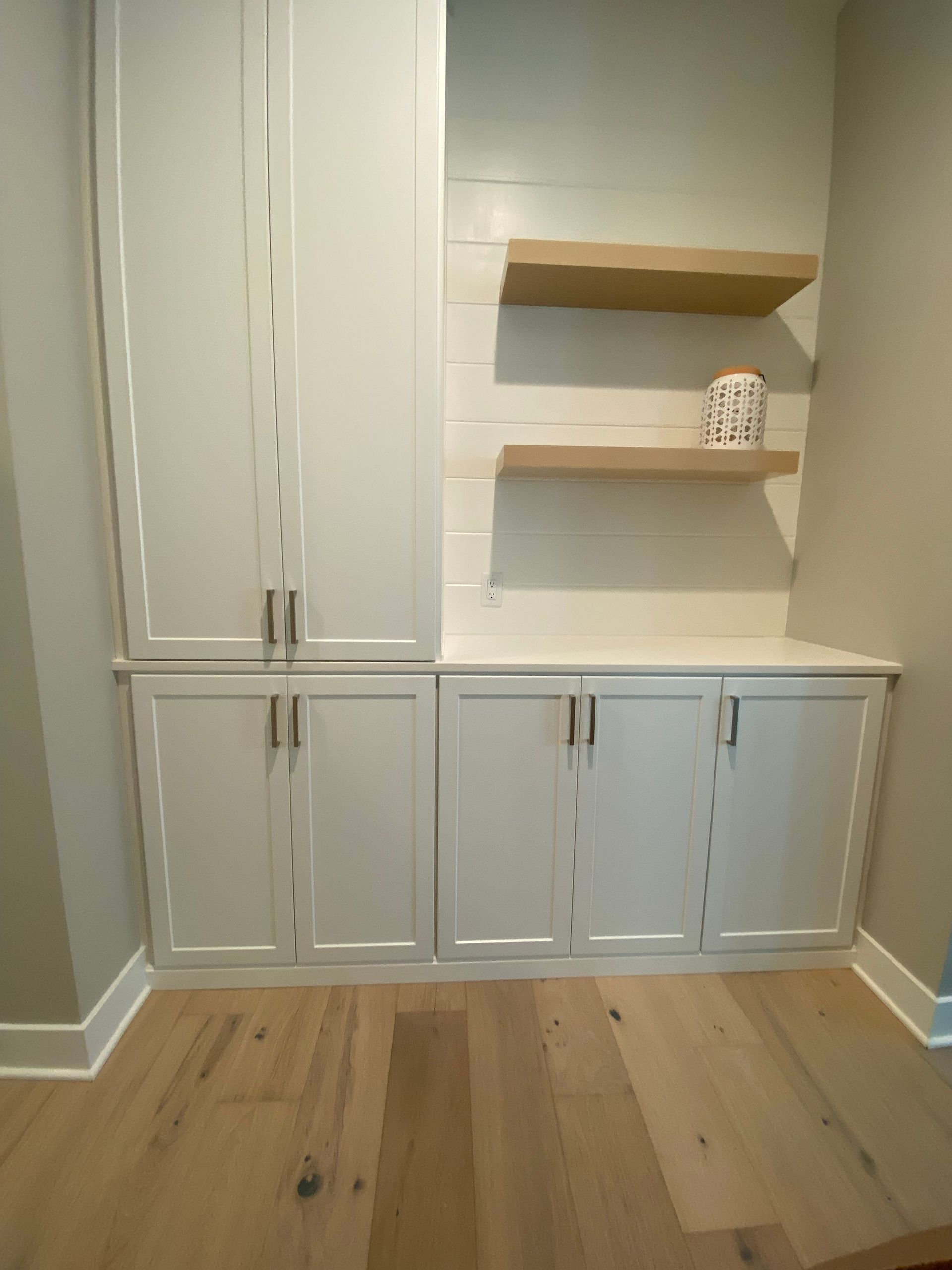 a nook with white cabinets and wooden shelves .