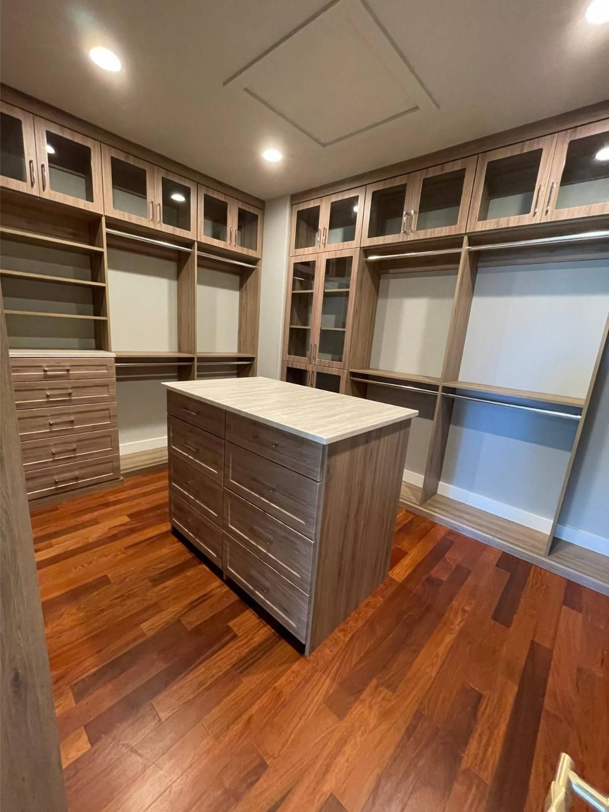 A walk in closet with hardwood floors and a large island in the middle.