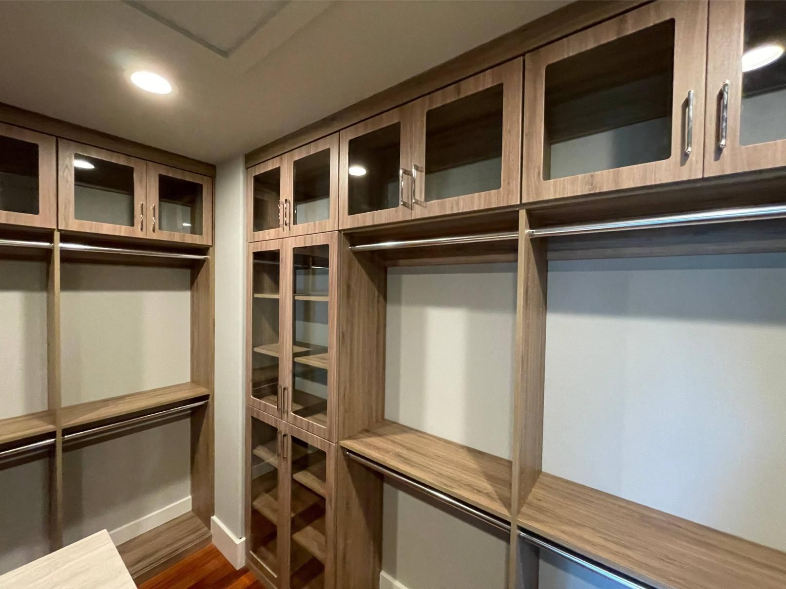 A walk in closet with wooden cabinets and glass doors.