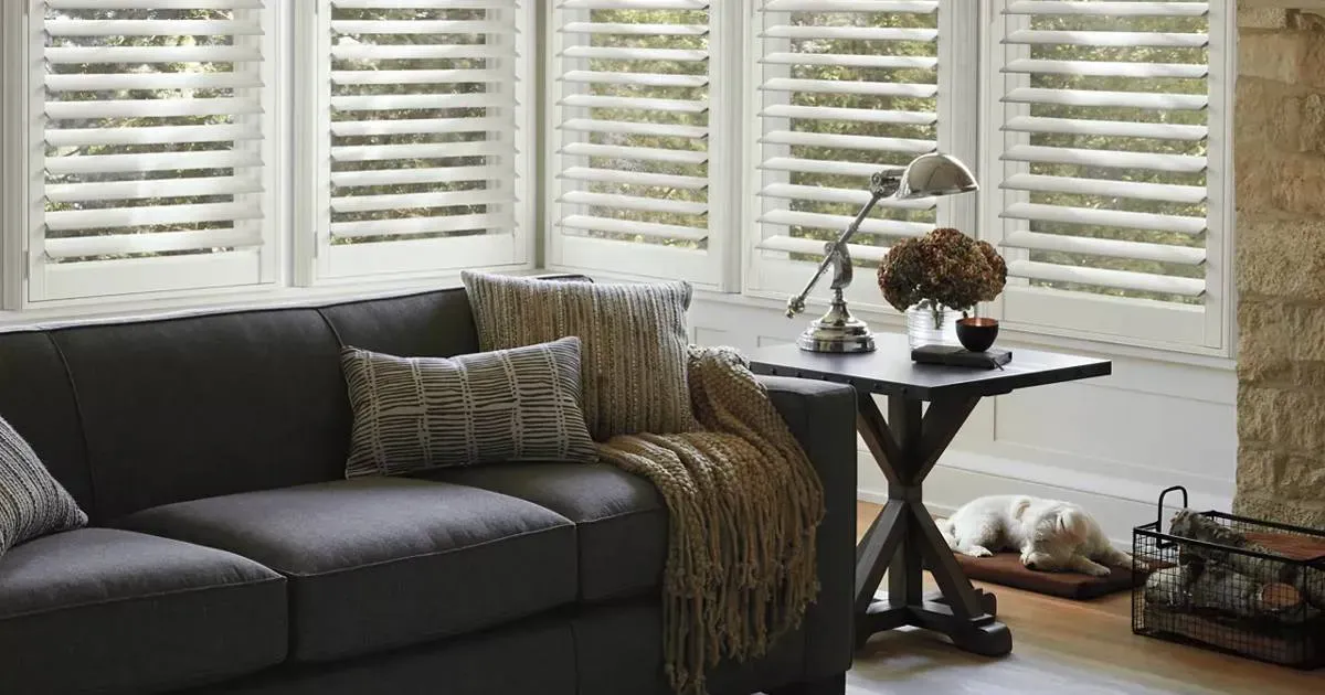 a dining room with a table and chairs, illuminated by natural light from window blinds.