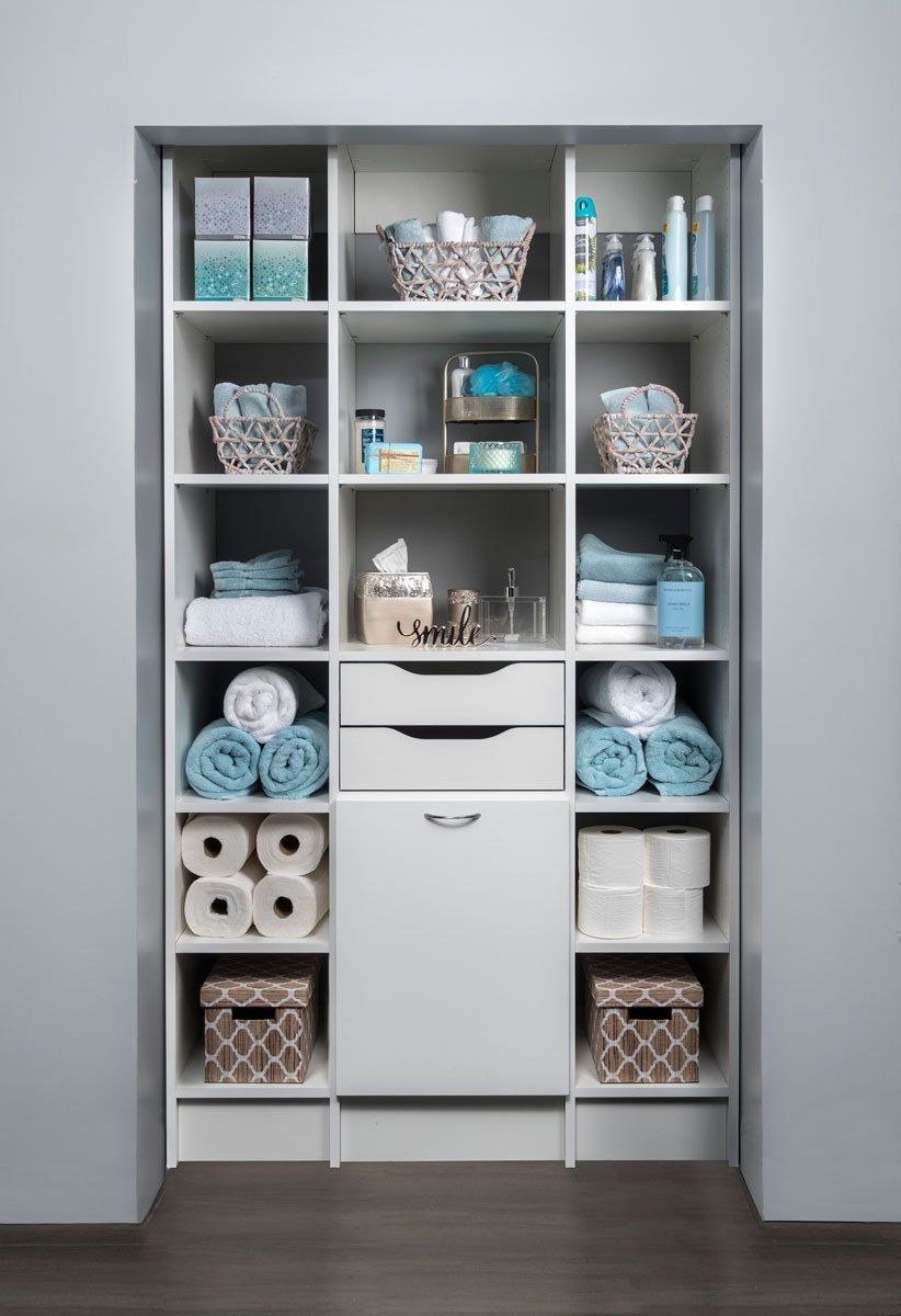 a bathroom closet filled with towels , toilet paper , baskets , and drawers .