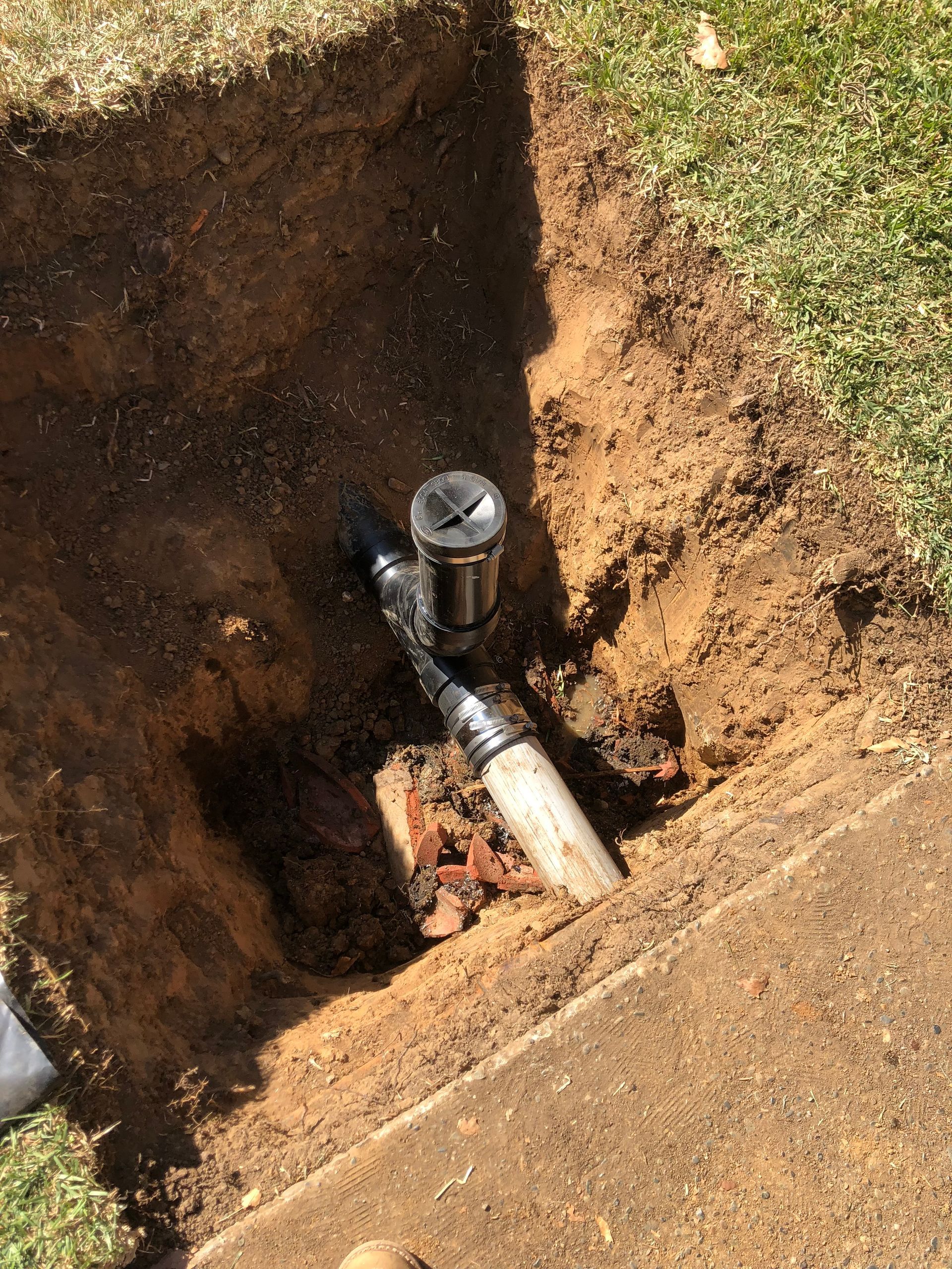 A pipe is laying in the dirt next to a sidewalk.