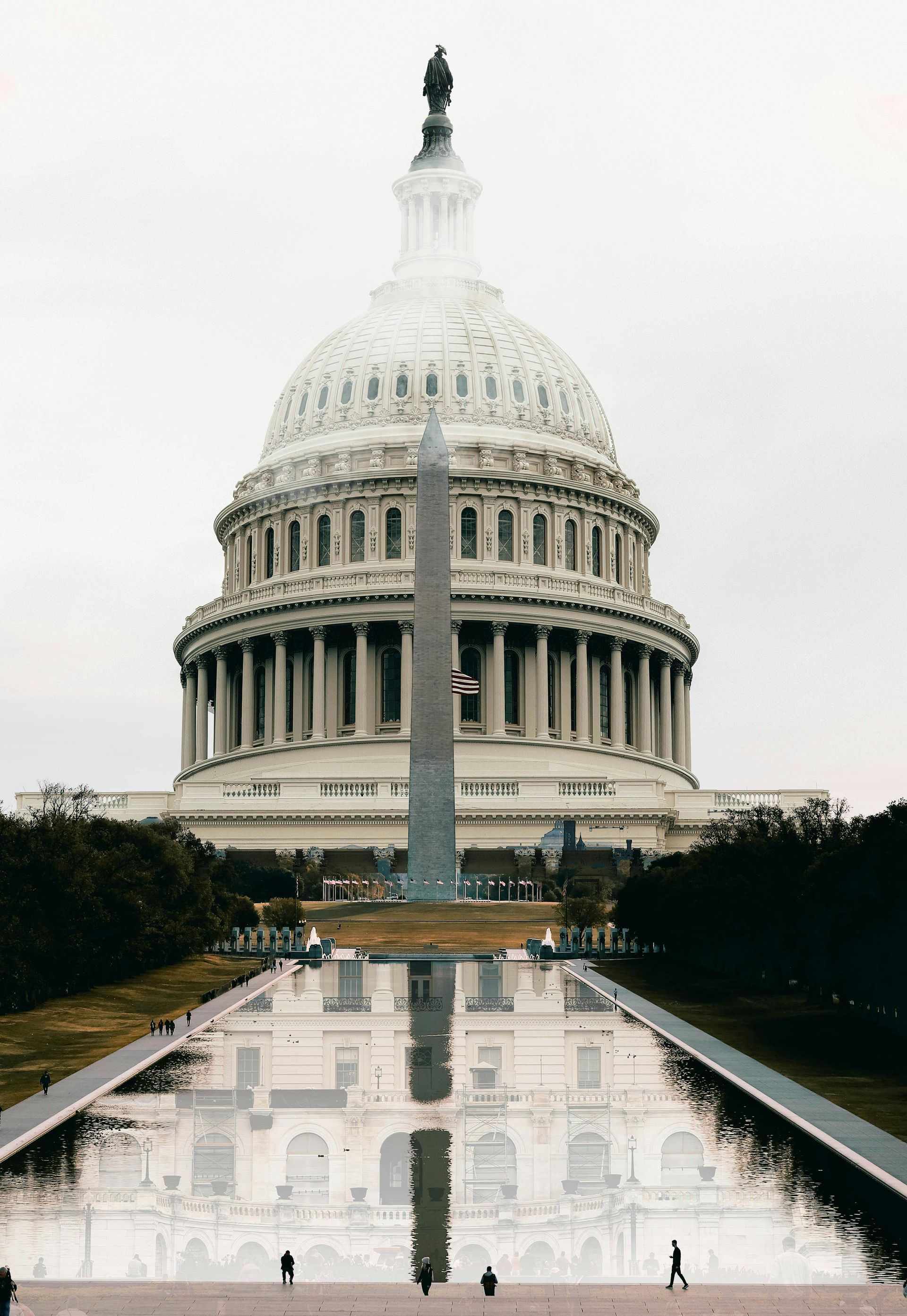 The U.S. Capitol Building with the Washington Monument reflected in a long pool of water.