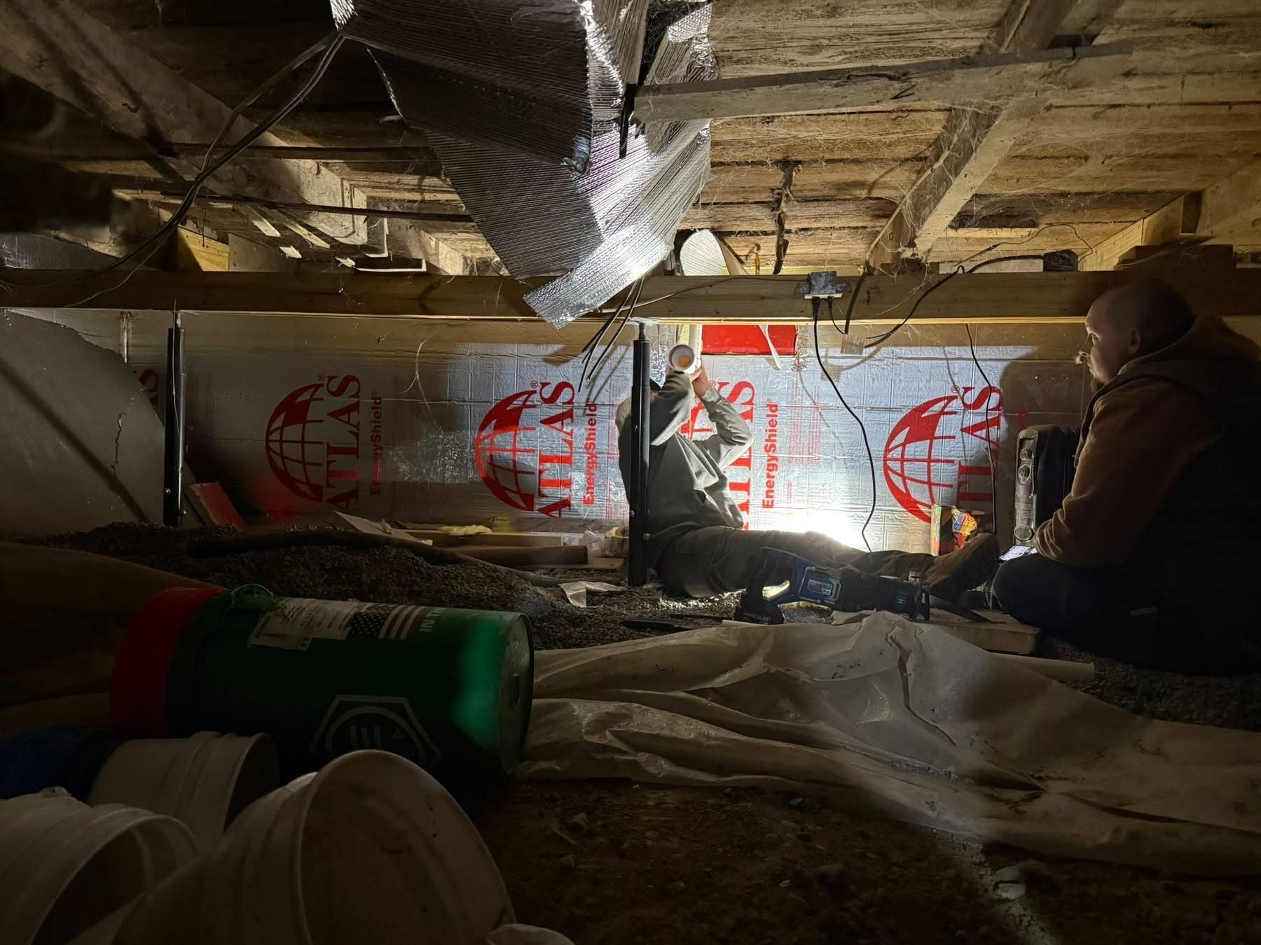 People working under a structure, possibly a house. They are inspecting or repairing something.