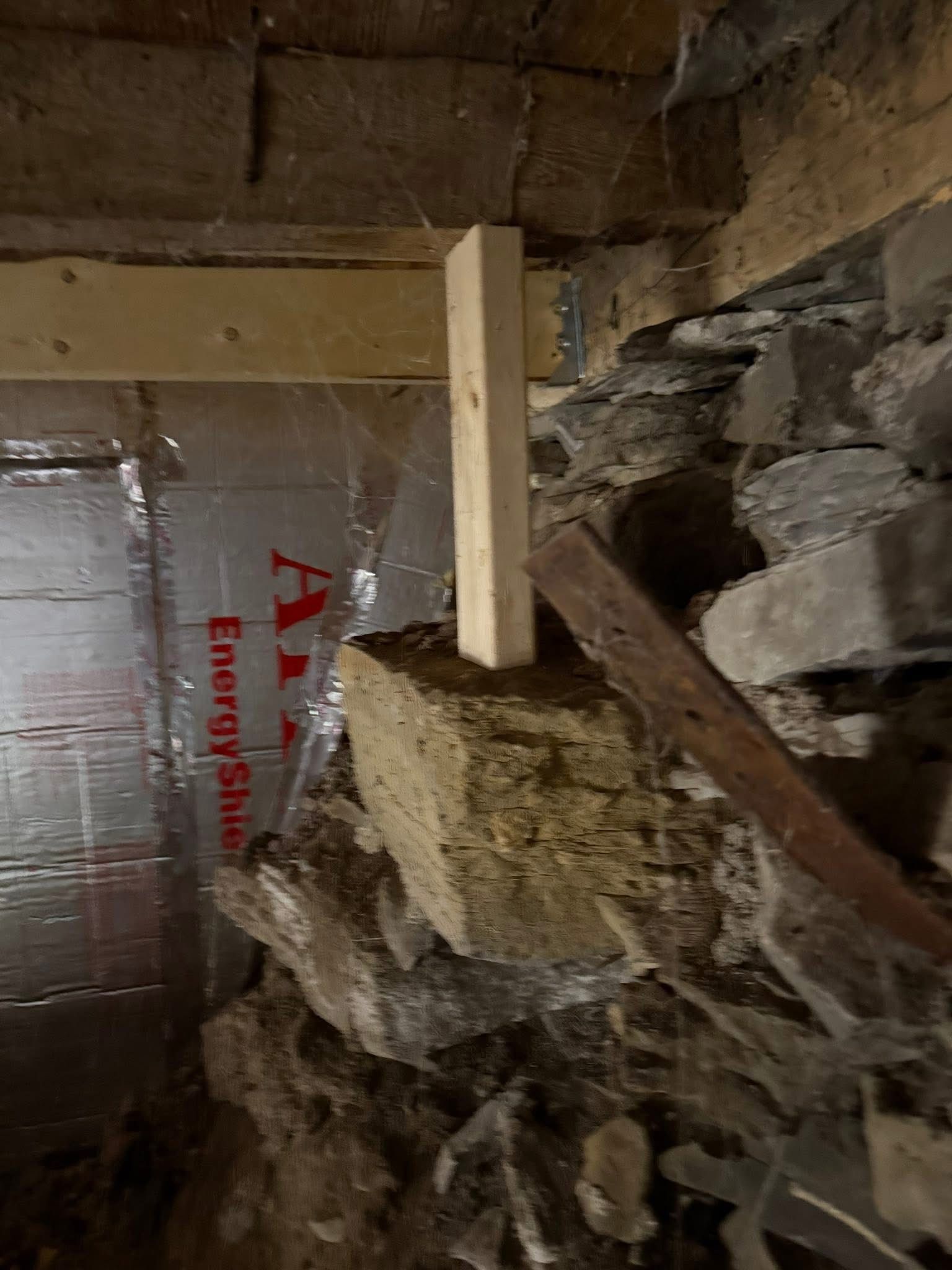 Wooden post supporting a crumbling stone foundation; interior with insulation and wood beams.
