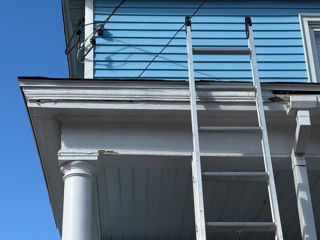 Ladder leaning against a blue house with white trim.