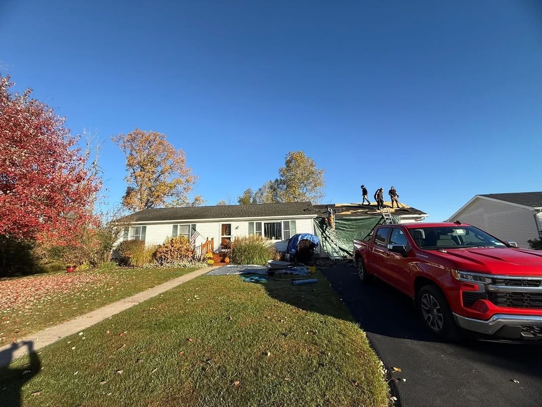 House with damaged roof and fire truck parked in driveway under blue sky.