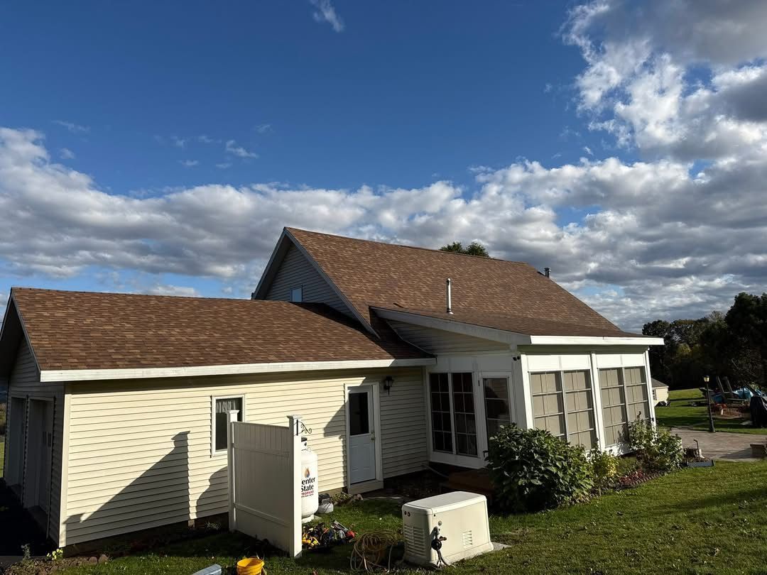 Beige house with brown roof against a partly cloudy blue sky. A screened-in porch is visible.