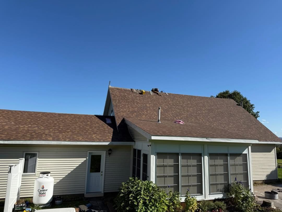 House with brown shingle roof, white siding, and screened-in porch under a blue sky.