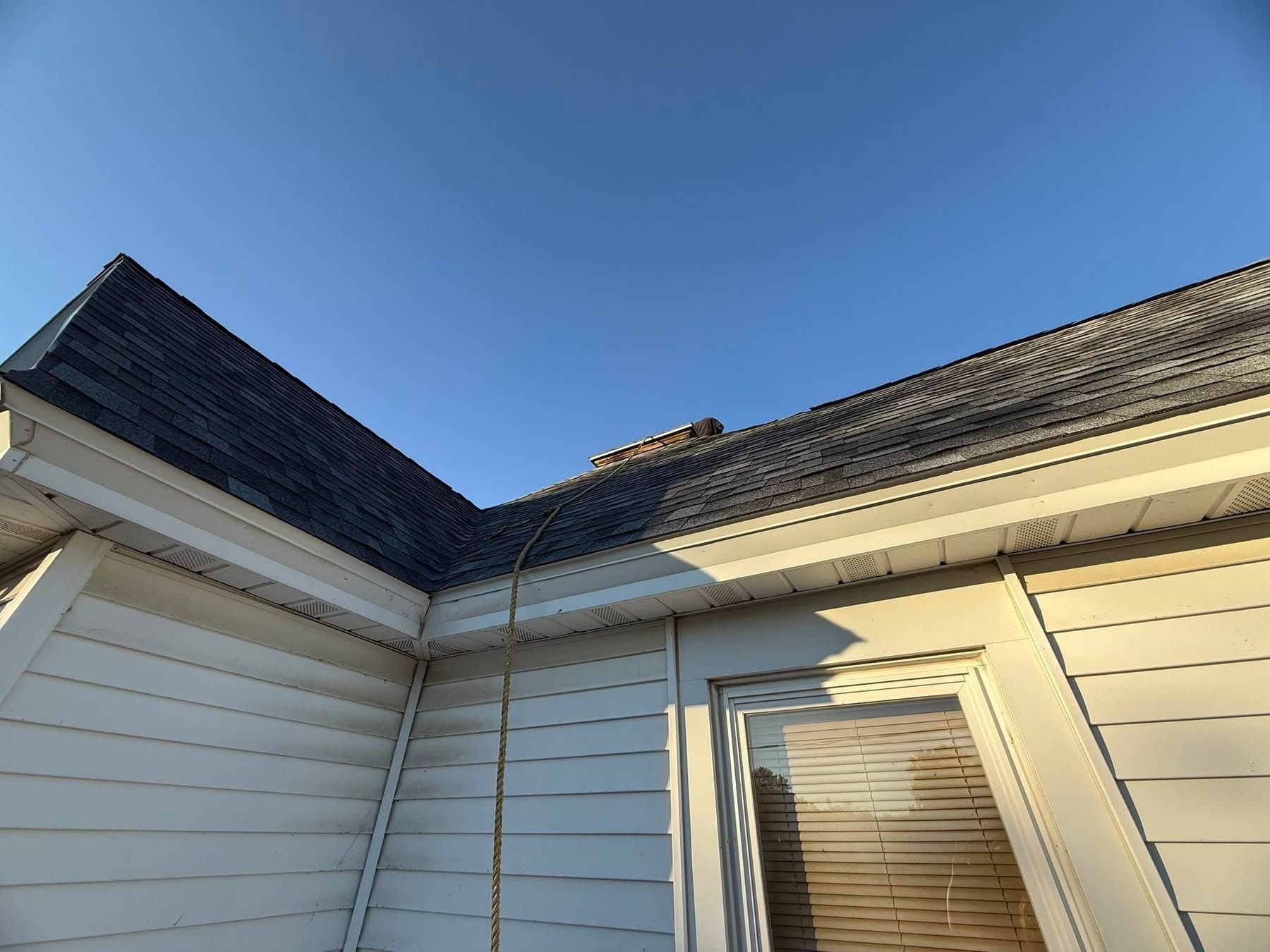 A low-angle view of a house roof and white siding against a blue sky.
