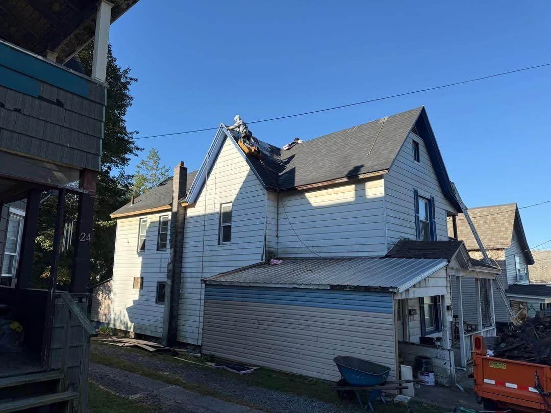 House with partial new roof under clear blue sky; asphalt shingles, white siding, power lines.