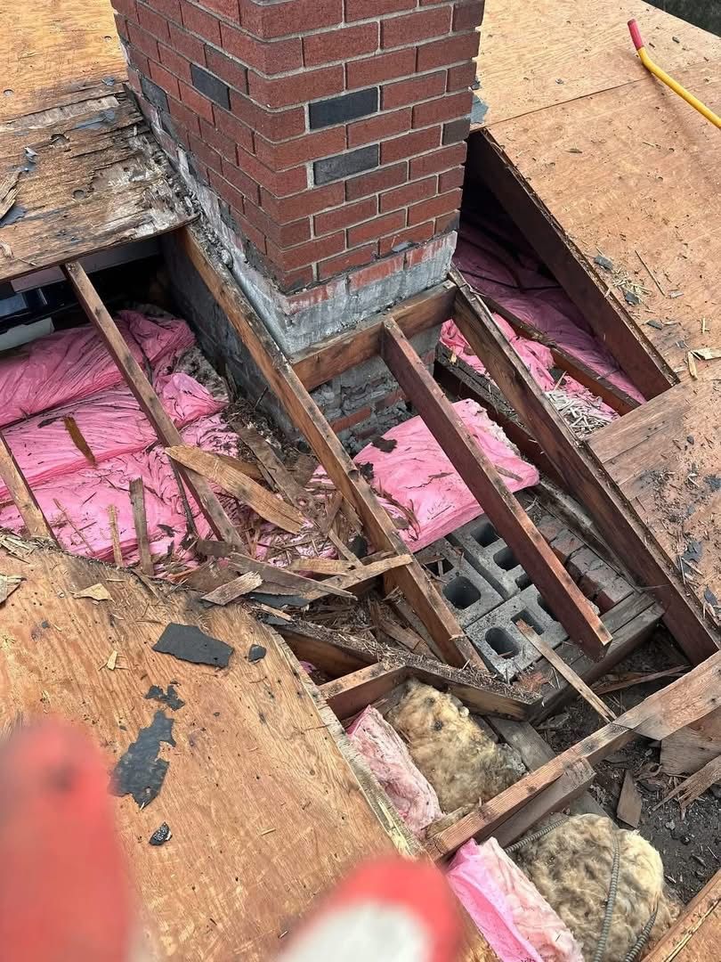 Damaged roof structure around a brick chimney, revealing insulation and framing.