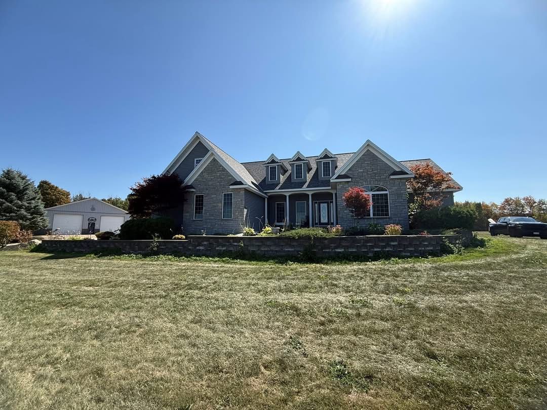 Large stone house with a lawn under a bright blue sky. A car is parked on the right.