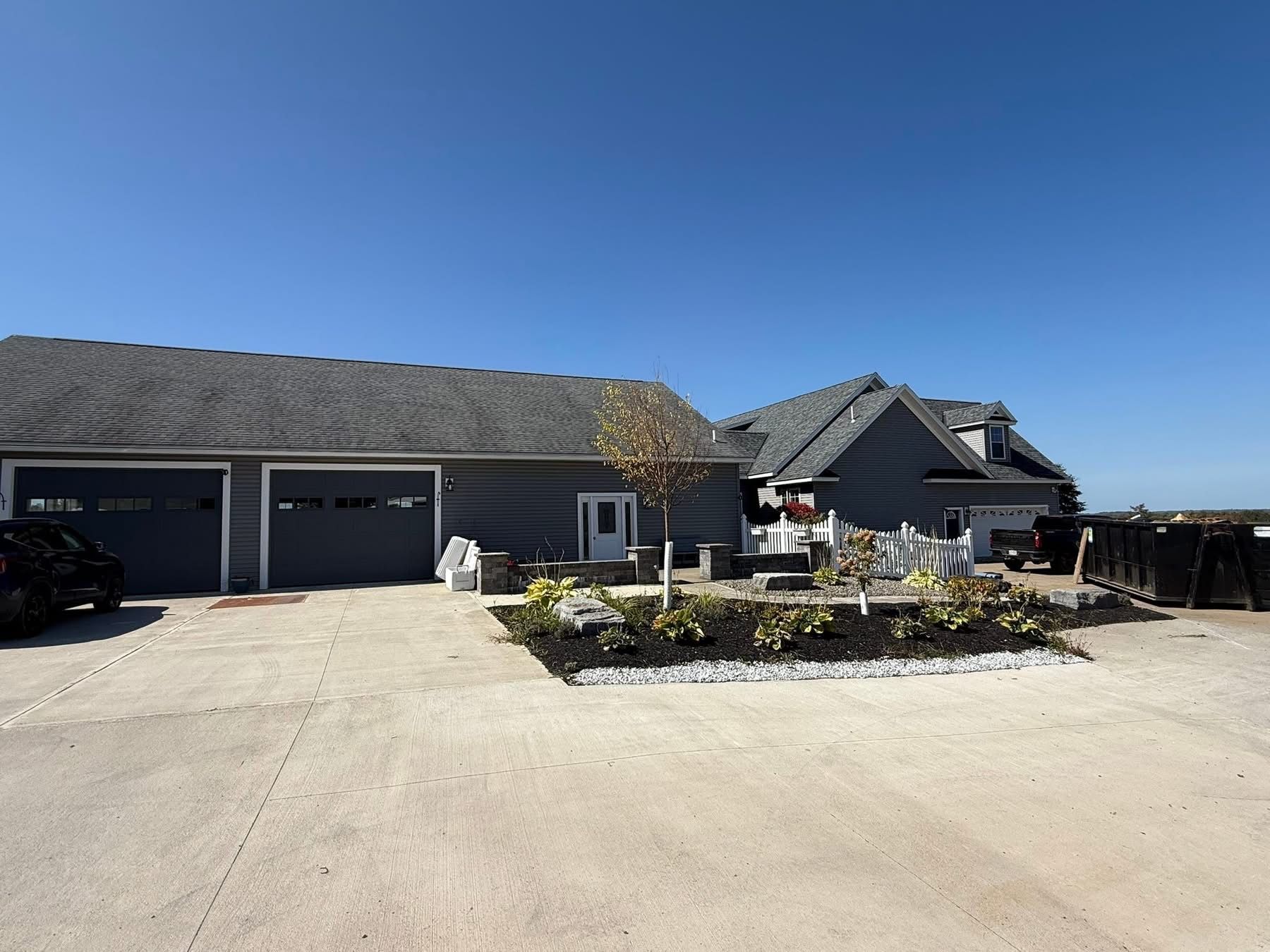Gray house with a two-car garage, gray roof, and landscaped yard on a sunny day.