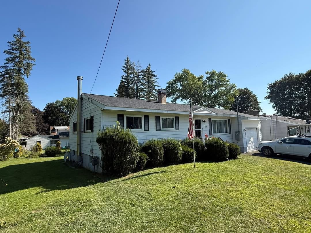White house with a green lawn, blue sky, and a car parked in front.