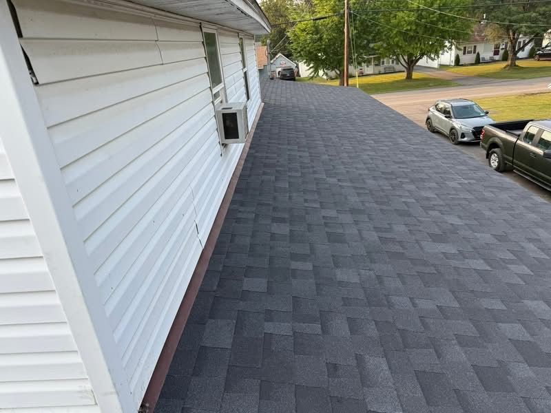 A house with a newly shingled gray roof and white siding. A car and truck are parked nearby.