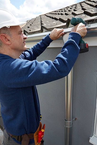 A man is using a drill to fix a gutter on a roof.