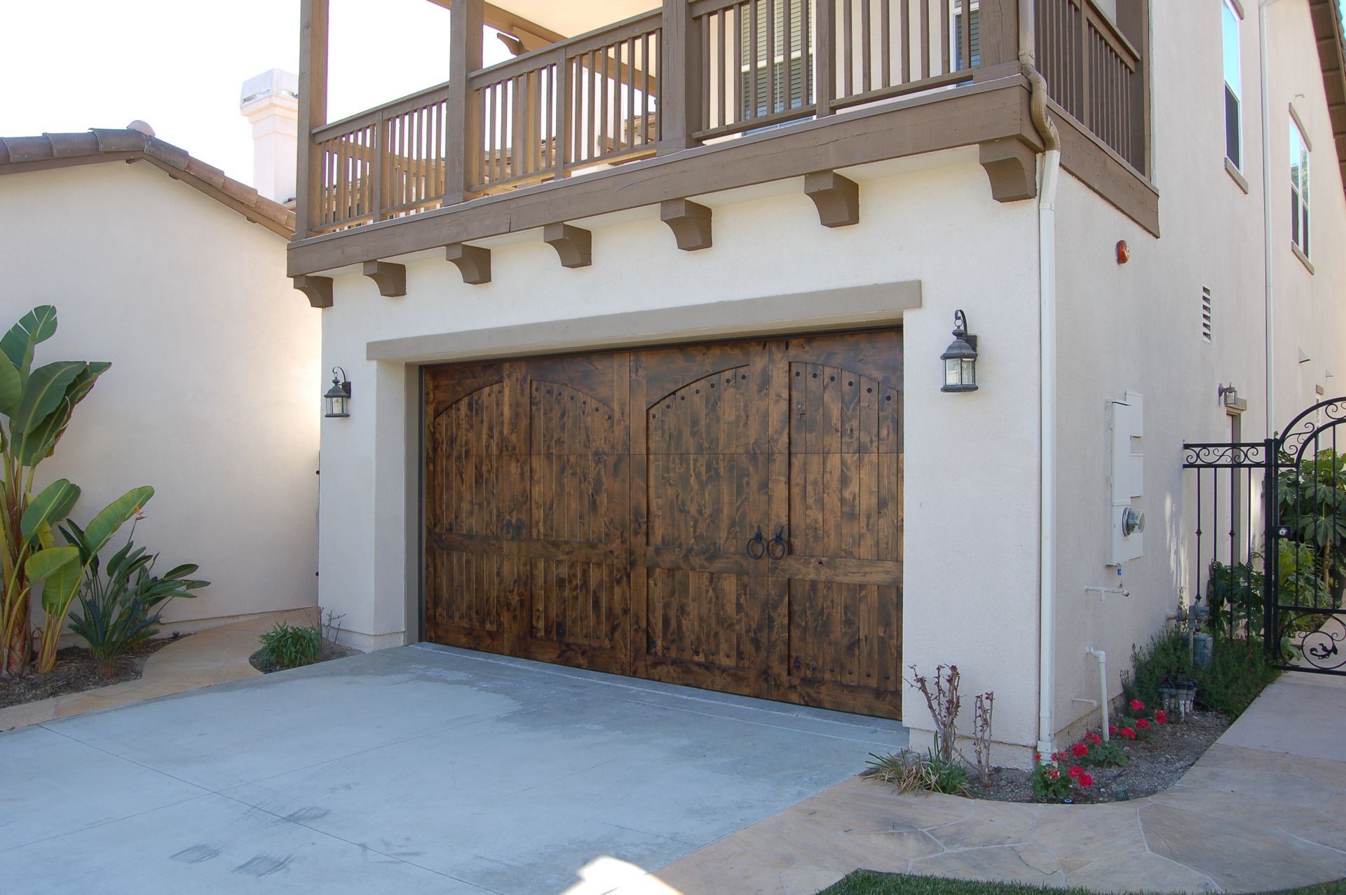 Mediterranean-style house exterior with wooden garage door, balcony, and driveway