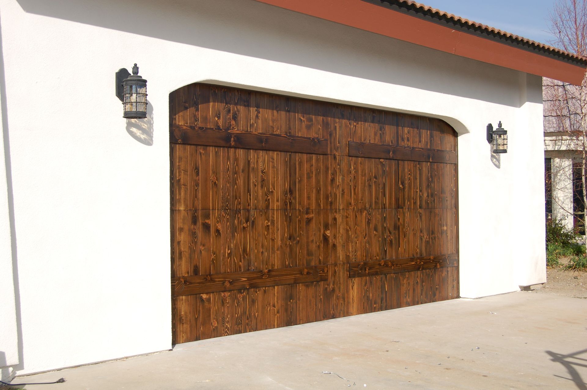 White stucco garage with large wooden double doors and wall lanterns under a tiled roof.