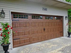 Brown wooden garage door with small windows, flanked by potted flowers on a driveway.