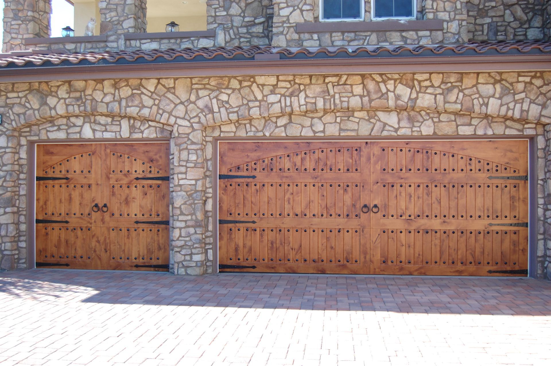 Stone house facade with two large wooden garage doors and paved driveway