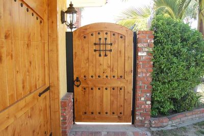 Wooden garden gate with arched top beside a brick wall and greenery