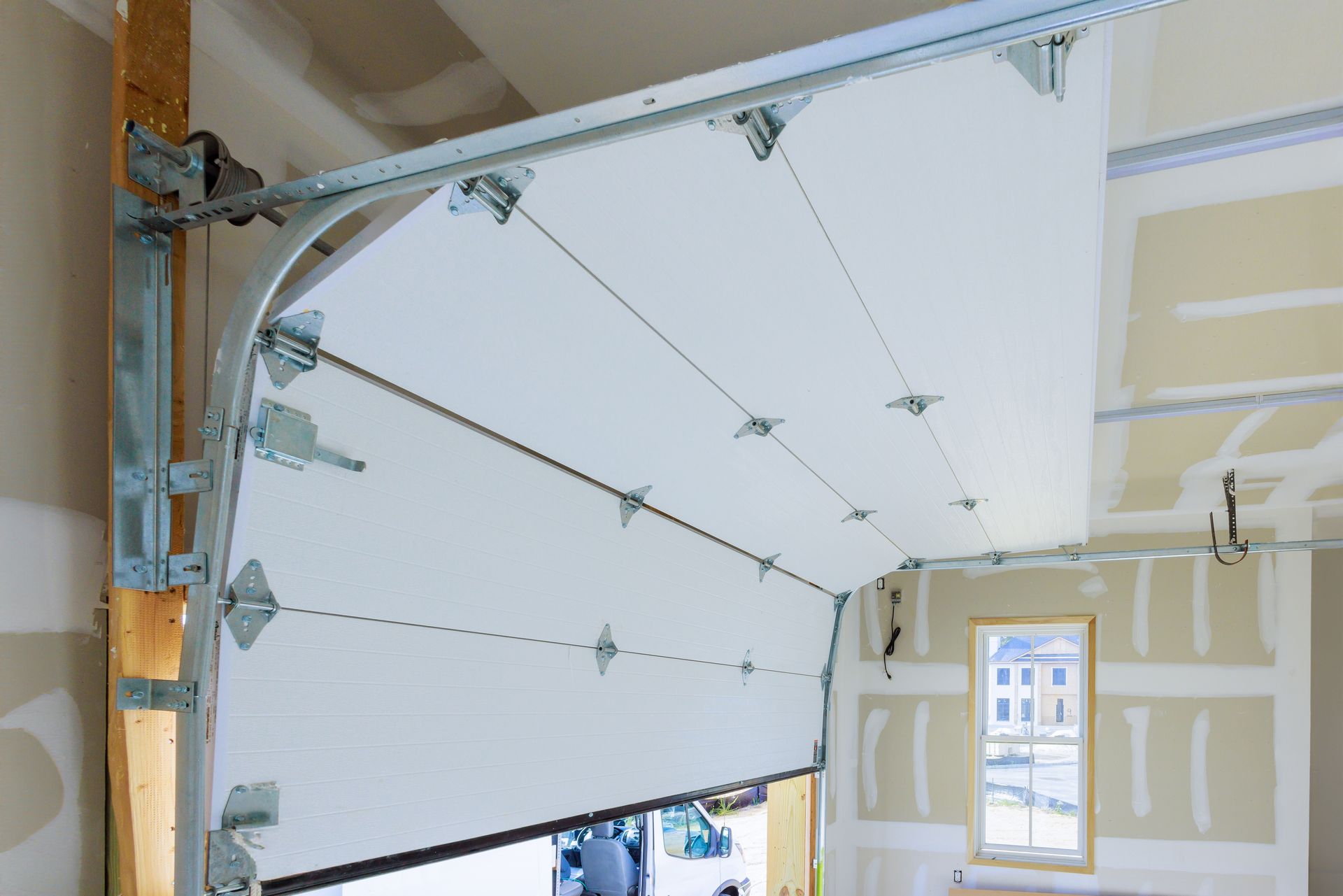 Partially open white garage door inside an unfinished room with exposed framing and drywall patches