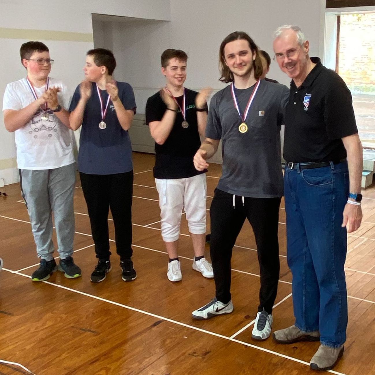 Seven young men wearing ribbons and medals stand next to their fencing coach, an older man.