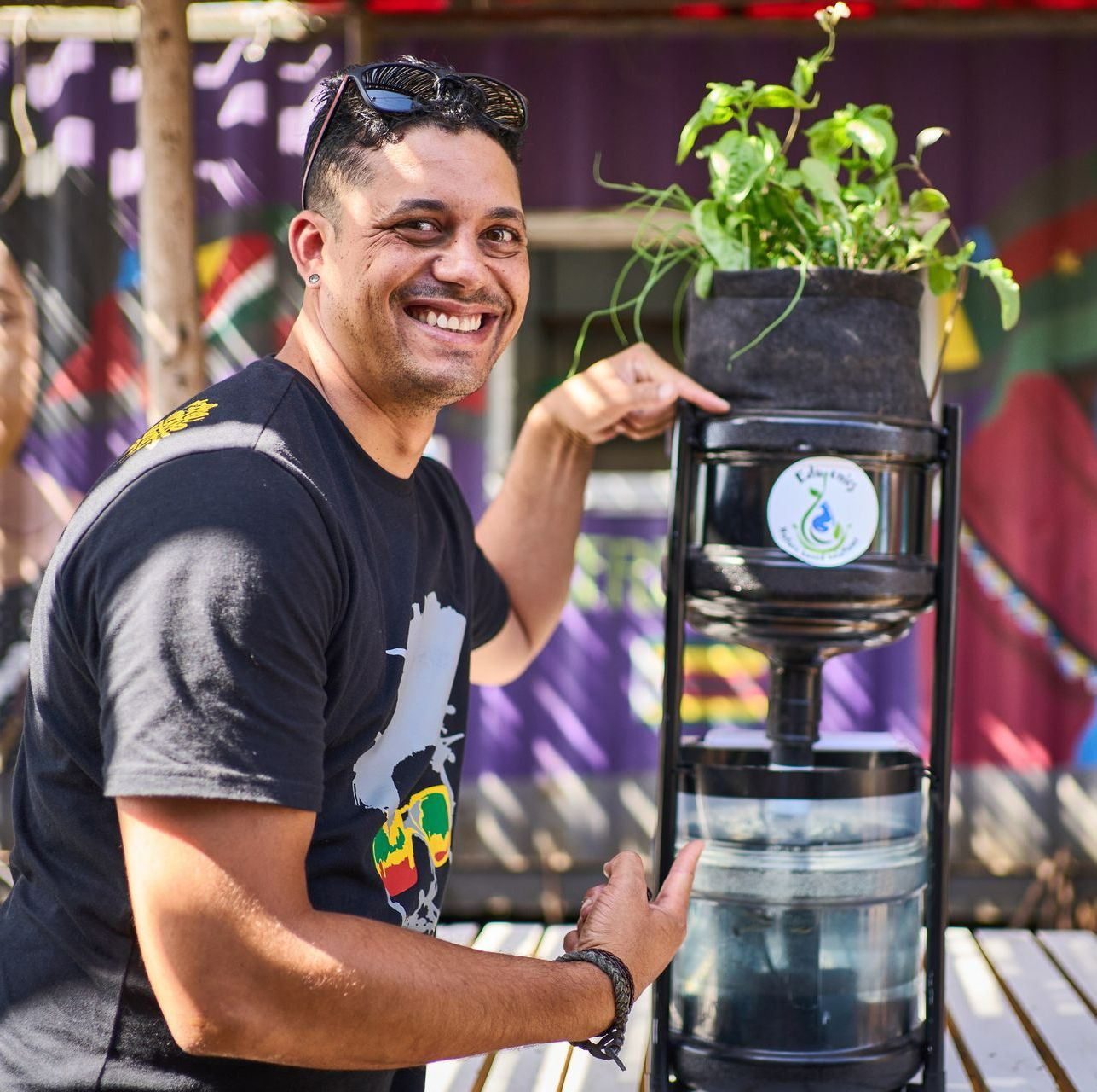 A man in a black shirt is smiling while holding a potted plant