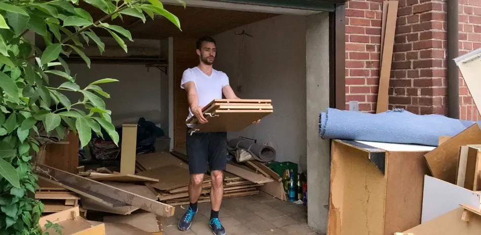 A man is carrying a piece of wood in a garage.