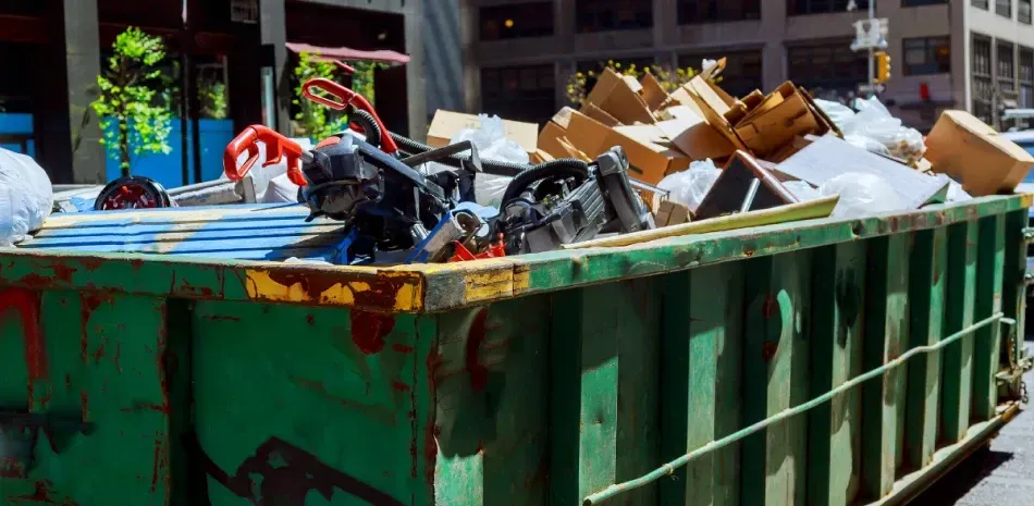 A large green dumpster filled with lots of trash on a city street.