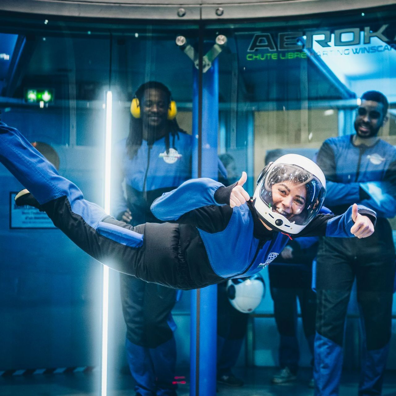 Une femme vole dans les airs tout en portant un casque et en levant le pouce
