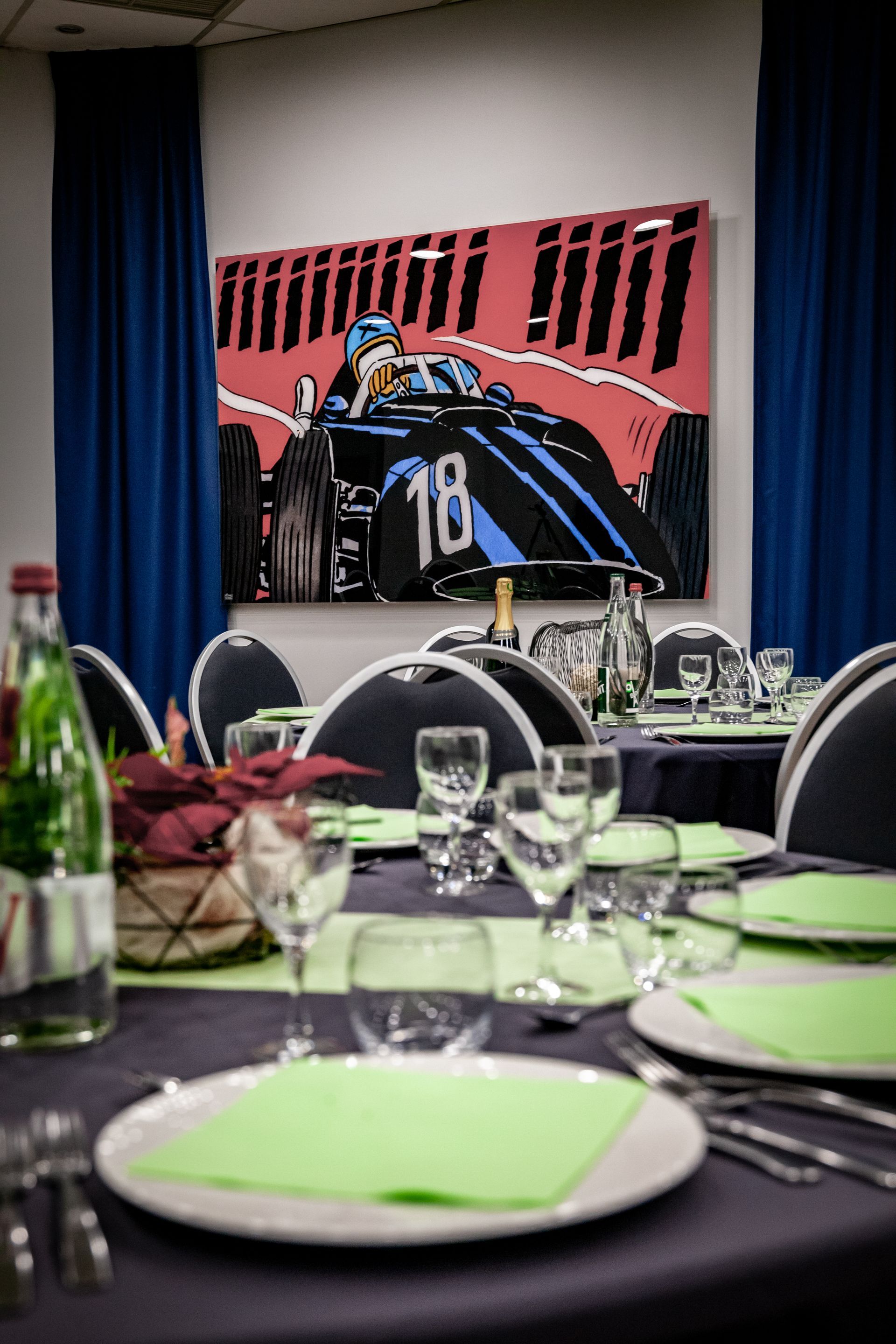 Une table dressée pour un dîner avec une peinture d'une voiture de course sur le mur derrière.