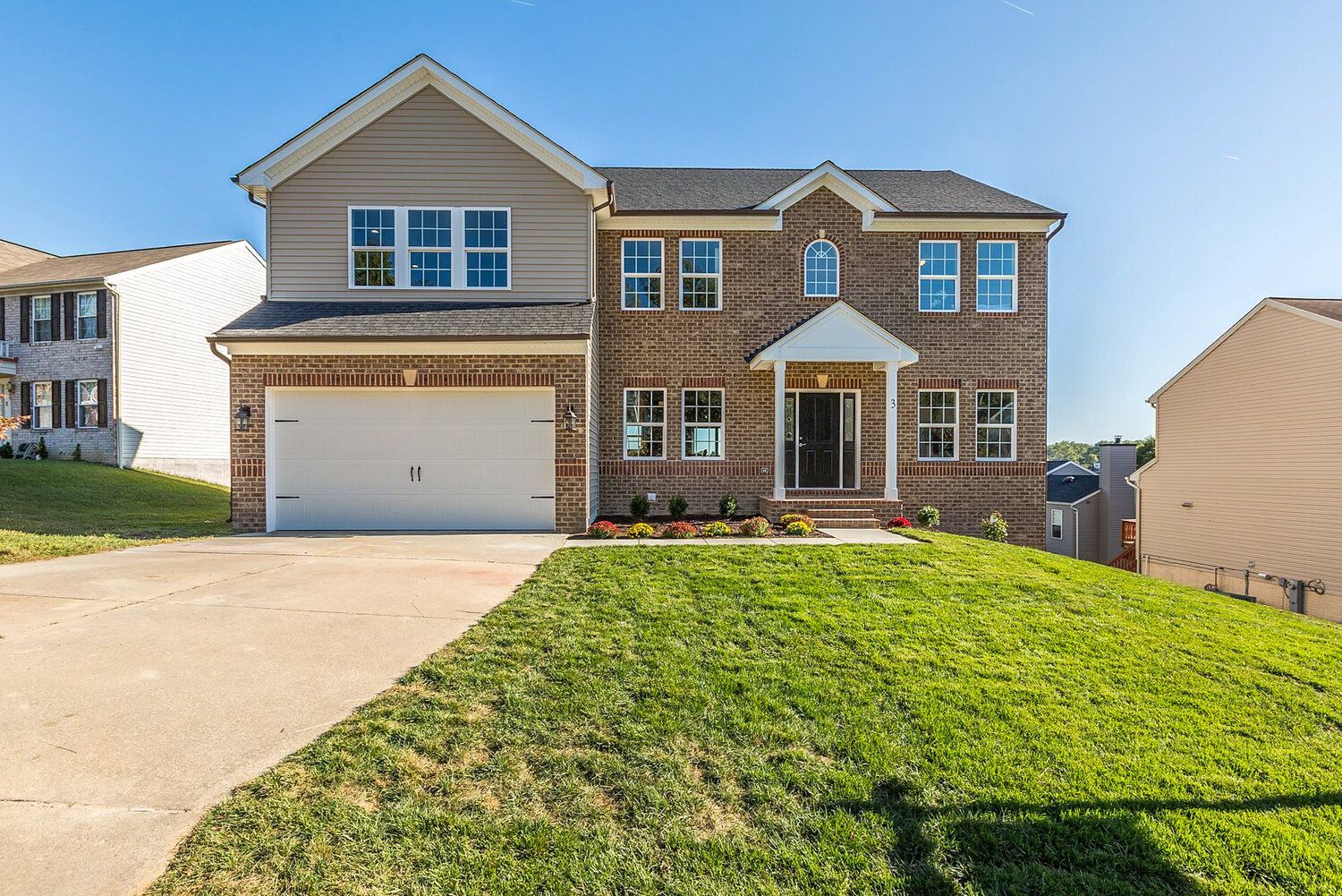 A large brick house with a white garage door is sitting on top of a lush green hill.